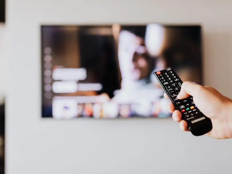 Hand riktar en fjärrkontroll mot en TV med appmeny